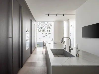A modern minimalist kitchen featuring concrete and marble materials, with a white marble countertop and dark wooden cabinets.