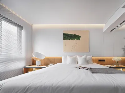 Modern minimalist bedroom with white walls, wooden headboard, and a green plant in a white pot.