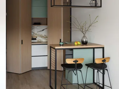 A modern kitchen with wood and metal finishes, featuring a bar table with stools and a vase with pears on the table.