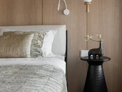 Modern minimalist bedroom featuring a bed with white bedding and pillows, a black side table with a vase and branch, and a wo