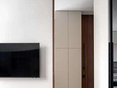 A modern minimalist bedroom with a wood laminate floor and a flat-screen TV on the wall.
