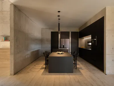 A modern, minimalist kitchen with concrete walls and black metal accents.