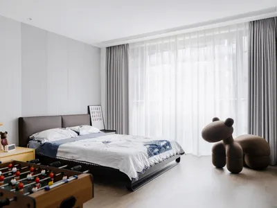A minimalist bedroom featuring wooden furniture and a large window with sheer curtains.