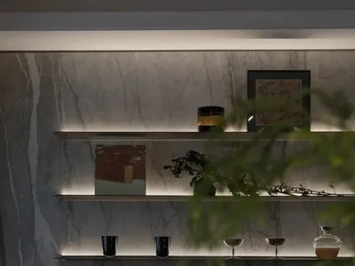 A sleek, modern bar counter featuring a combination of marble and glass materials, with shelves displaying decorative items.