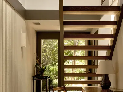 A modern home office with wooden furniture and stone flooring, featuring a built-in desk, chair, and large window.