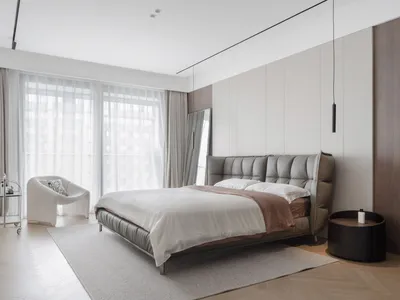 Modern minimalist bedroom with a leather bed and fabric headboard, featuring large windows with sheer curtains and a sleek si