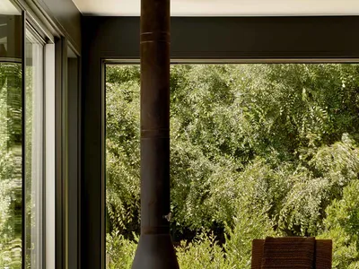 A cozy, industrial-style living room featuring a metal wood stove and a comfortable armchair surrounded by lush greenery.