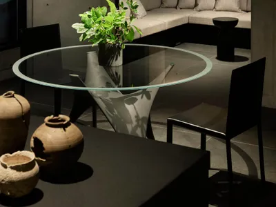 A minimalist living room featuring a concrete wall, circular glass table, and black chairs.