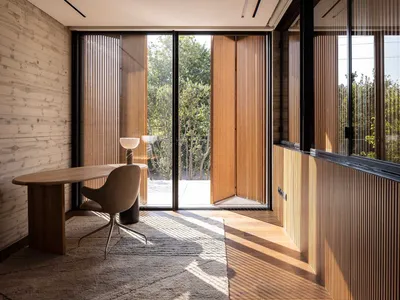 A minimalist home office with wooden paneled walls, a round wooden desk, and a modern, round floor lamp.