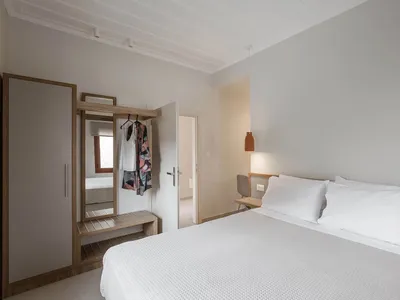 Minimalist bedroom with a white bed, wooden headboard, and simple decor.