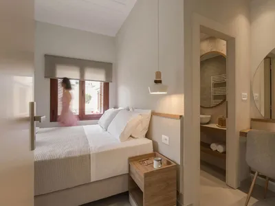A minimalist bedroom with a white and neutral color theme, featuring a bed, nightstand, and bathroom access