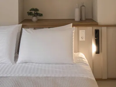 A minimalist bedroom featuring a bed with white bedding, a wooden headboard, and concrete shelves with books and decorative i