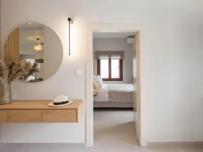 A minimalist bedroom featuring a wooden desk and white walls, with a view into the adjoining room.