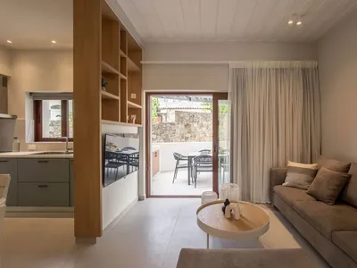 A modern, minimalist living room with concrete walls, wooden furniture, and a flat-screen TV mounted on the wall.