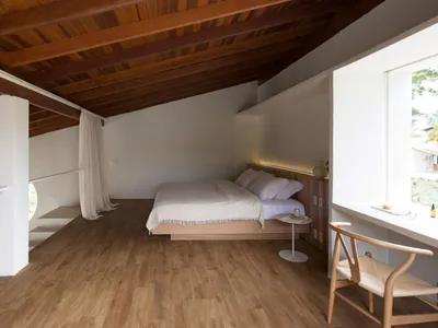 Modern minimalist bedroom with wooden floor and furniture, high ceiling with exposed beams.