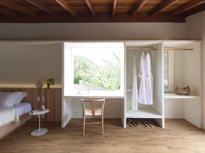A minimalist bedroom with a large window, a wooden chair, and a view of an indoor garden.