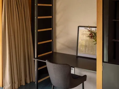 A minimalist home office featuring a black desk, grey chair, wooden shelves, and a framed piece of art.