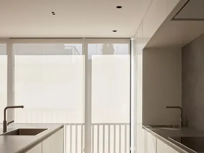 一間現代簡約風格的廚房，配有俐落白色櫥櫃與一扇可俯瞰陽台的大型窗戶。
