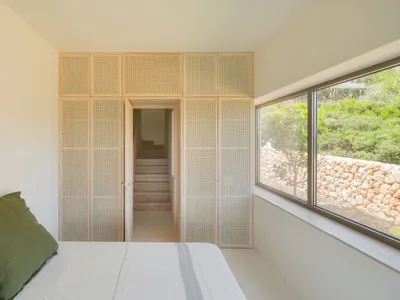 Minimalist bedroom featuring wooden furniture and a large window overlooking greenery.