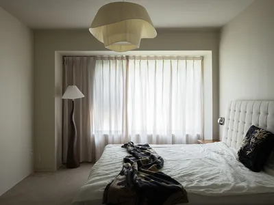 A minimalist bedroom with light-colored walls, a bed with a tufted headboard, and curtains.