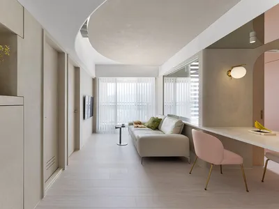A minimalist living room with concrete walls, a white sofa, and a pink chair.