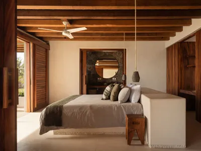 A minimalist bedroom with a low bed, wooden flooring, and a ceiling fan.