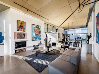 Modern minimalist living room with concrete walls and floor, featuring a large sofa, coffee table, fireplace, and abstract ar
