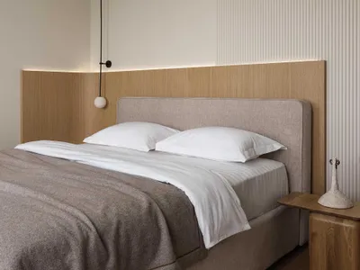 Minimalist bedroom with a wooden headboard, white bedding, and a side table with a white sculpture.
