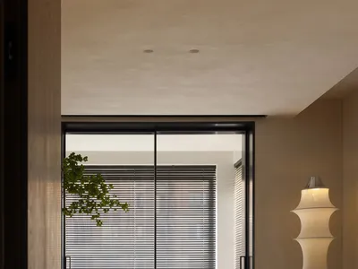 A minimalist home office featuring a wooden desk and chair in front of a window with blinds.