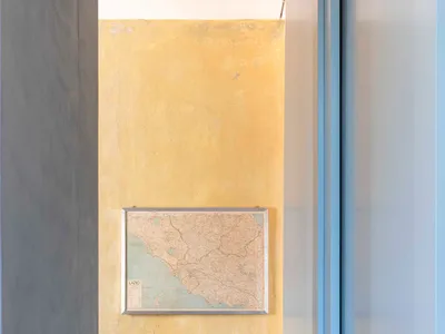 A modern home office with yellow painted walls, a map of Italy on the wall, a single wooden-framed cushioned chair, and a pat