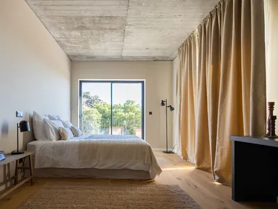 A minimalist bedroom with beige walls, a wooden floor, and a large bed with white bedding and pillows.