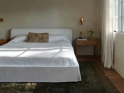 極簡臥室內擺放白色床鋪與質感布料，搭配簡約床頭櫃及花瓶插花。
