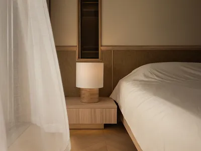 A minimalist bedroom featuring a wooden nightstand with a soft textile lampshade.