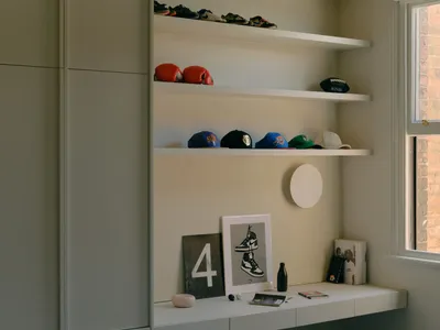 A minimalist bedroom with white shelves displaying various items like shoes, hats, and a poster of sneakers.