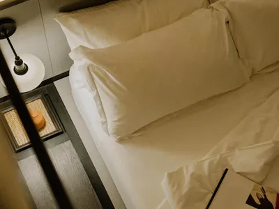 A neatly made white bed with pillows and a magazine on the mattress.