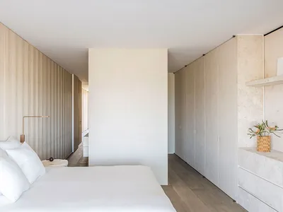 一間簡約臥室，擁有白牆、白色床具，以及木質床頭板。