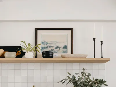 A modern, minimalist kitchen with black cabinets, concrete countertops, and a floating wood shelf above the sink.