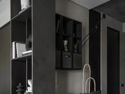 Close-up of a minimalist home office with black metal desk, chair, and shelving unit.