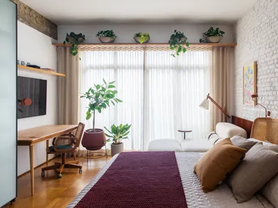 A minimalist bedroom featuring wooden furniture and textiles, with a large window allowing natural light.