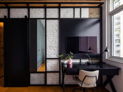 A modern home office with black furniture and a brick wall, featuring a desk, chair, and TV.
