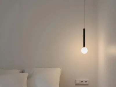 A minimalist bedroom featuring a white bed with curtains, a glass pendant light, and minimalistic furnishings.