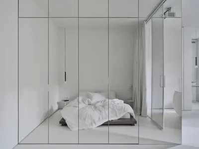 A minimalist bedroom with a white bed and white walls.