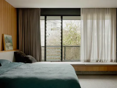 Modern minimalist bedroom featuring a floating bed, wooden headboard, and white sheer curtains framing a large window.