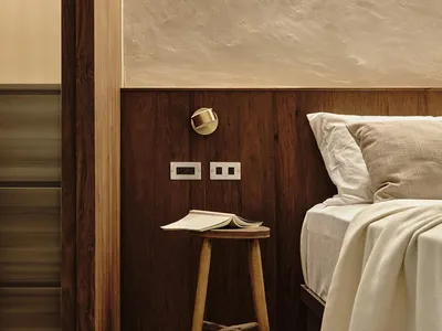 Minimalist bedroom featuring wood furniture and cement walls with a stool and book as focal points.