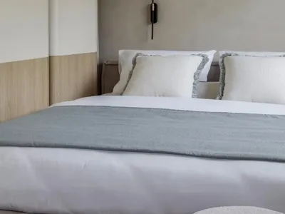 A minimalist bedroom with gray and white bedding, framed abstract art, and a modern fabric ottoman.