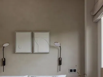 A minimalist bedroom with neutral-toned fabrics, white bedding, and art above the bed.