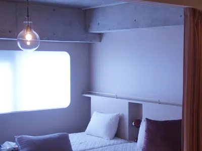 Minimalist bedroom with concrete walls, white bedding, and purple accent pillows.