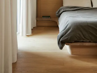 A minimalist bedroom featuring a wooden floor, bed with a wooden headboard, and simple wall-mounted lamp.