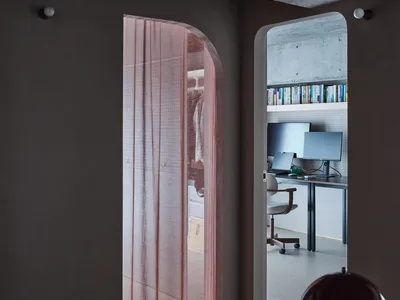 A modern home office with a pink curtain, computer desk, and bookshelf.