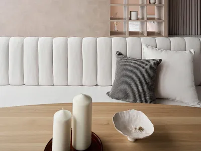 A minimalist living room with concrete walls, a white sofa, and a wooden coffee table with candles and bowls.